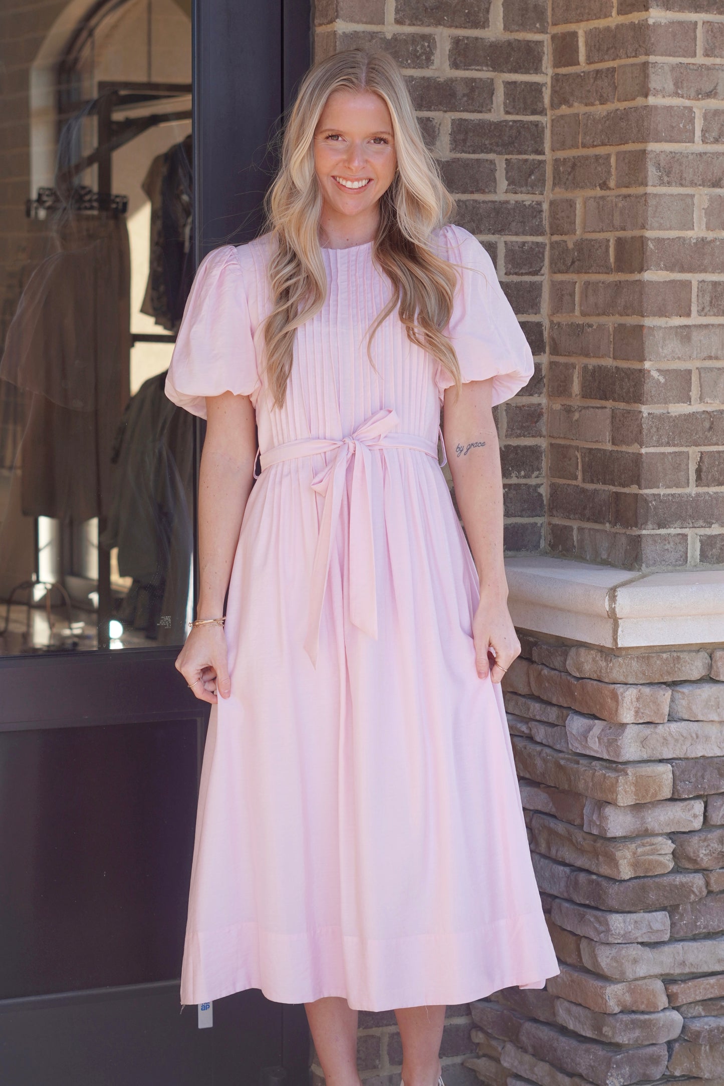Women wearing a baby pink maxi dress, short puff sleeves, belt, round neckline. 