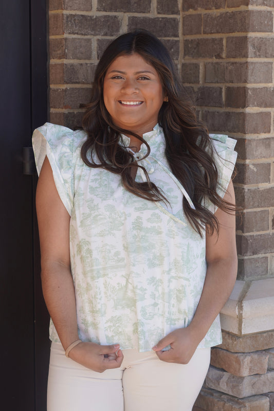 women wearing a green toile print with white base blouse, v neckline with a ruffle collar, ruffled short sleeves, flowy.