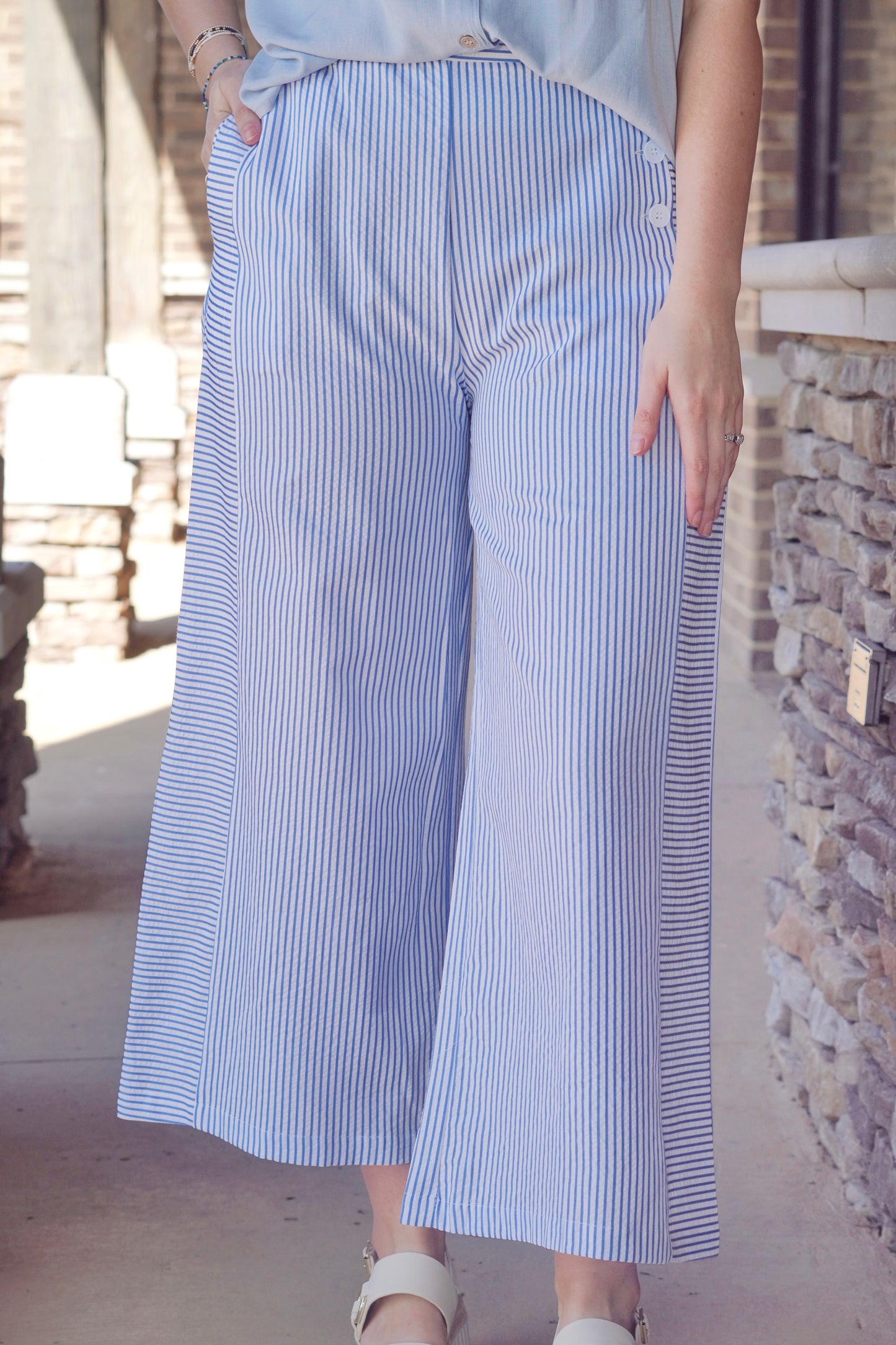 Blue thin striped pants with a white base, wide leg, buttons on the side pocket and elastic waist band 
