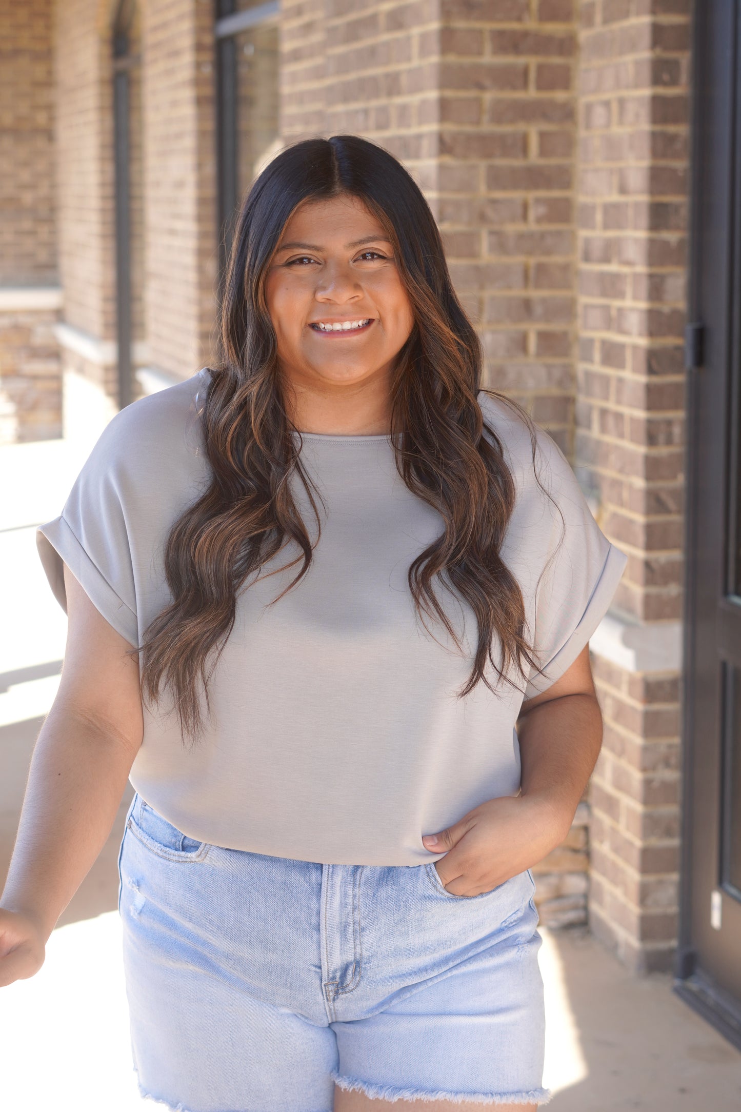 Woman wearing a short sleeve grey top with a round neckline and rolled sleeves paired with blue jeans