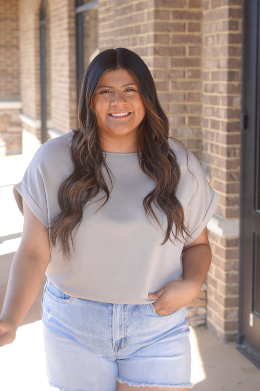 Woman wearing a short sleeve grey top with a round neckline and rolled sleeves paired with blue jeans