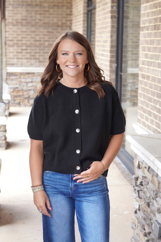 Women wearing a black sweater top, short sleeve, buttons going down the front, round neckline