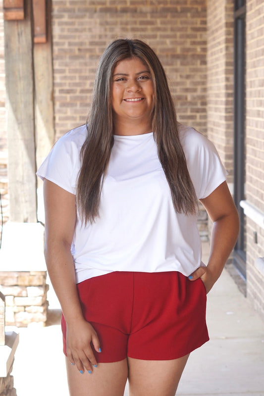 Women wearing a white short sleeve top, flowy, round neckline, paired with some red shorts. 