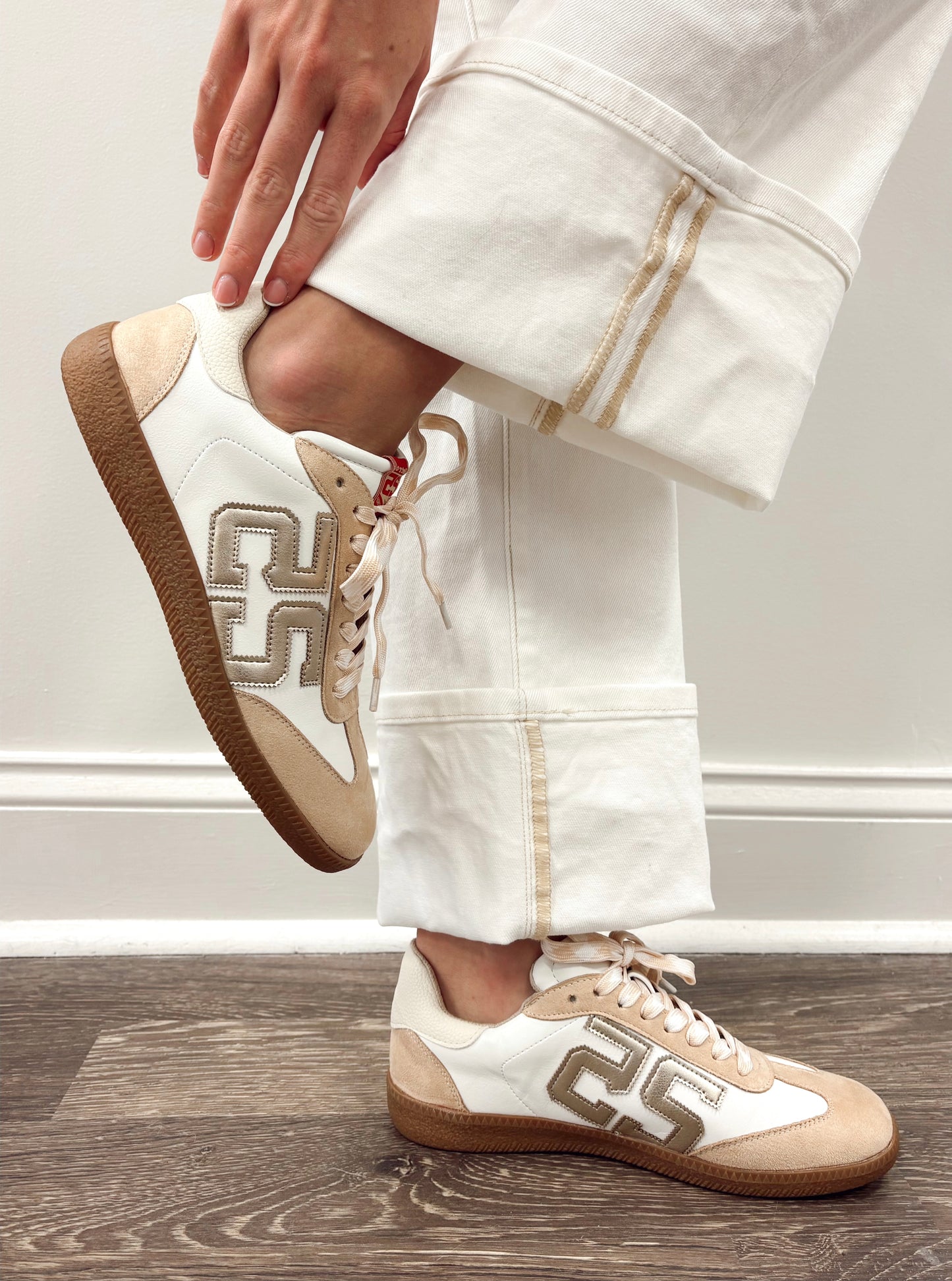 Model wearing Tan and White sneakers with a Retro Style Design on the side, along with small Gold Details