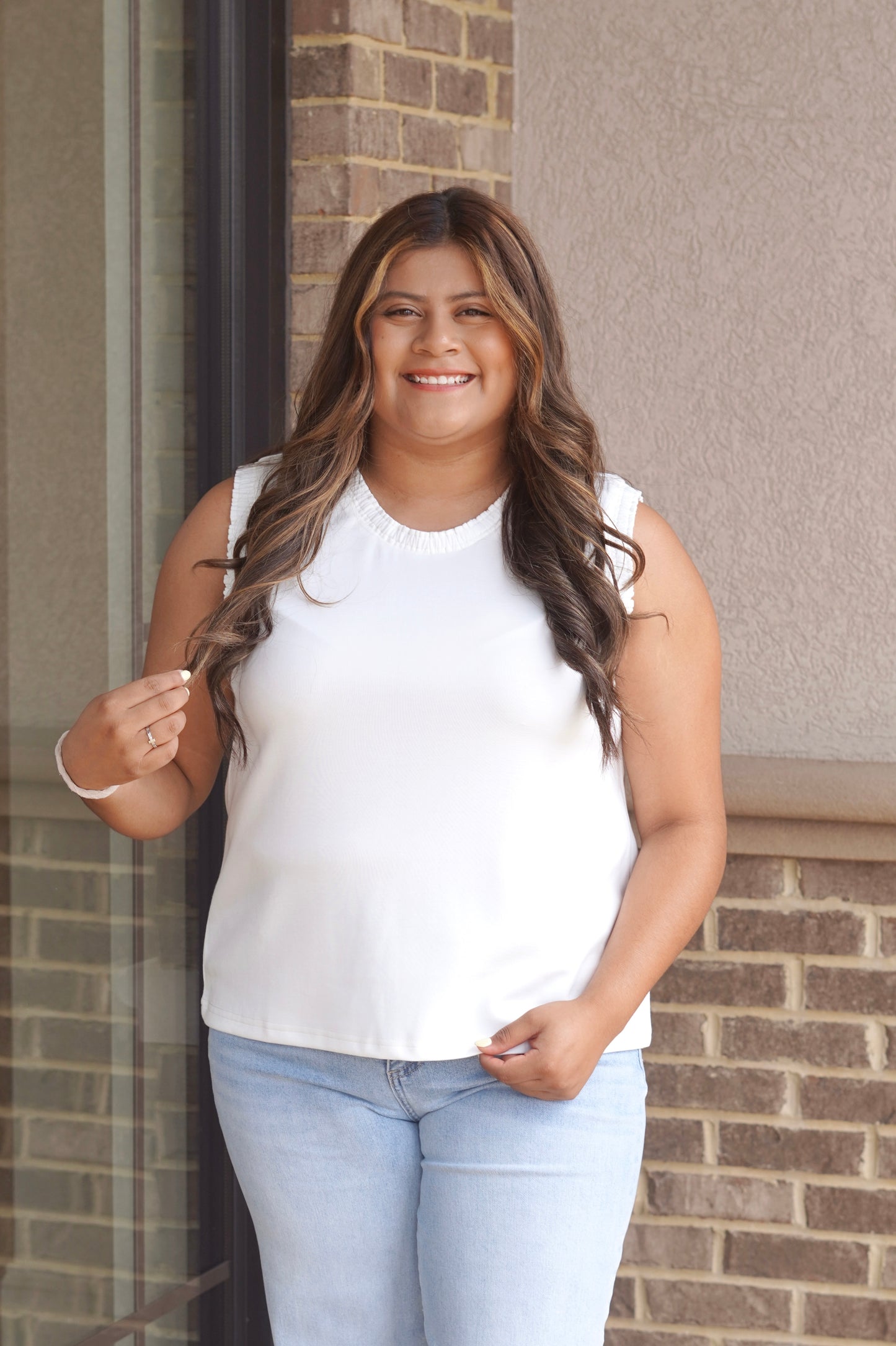 Women wearing a white tank top that has a ruffle trim in the neckline as well as the sleeves, sleeveless, round neckline.