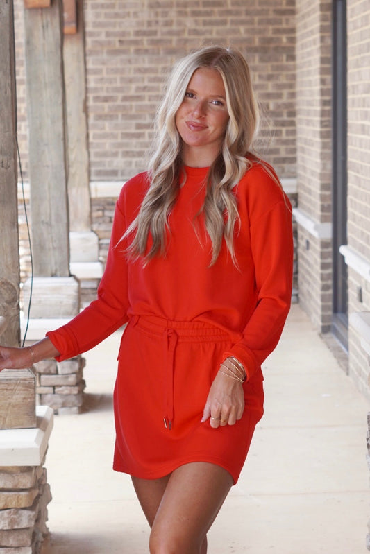 Women wearing a red skort, mid thigh length, with a drawstring waist band, paired with a red long sleeve top. 