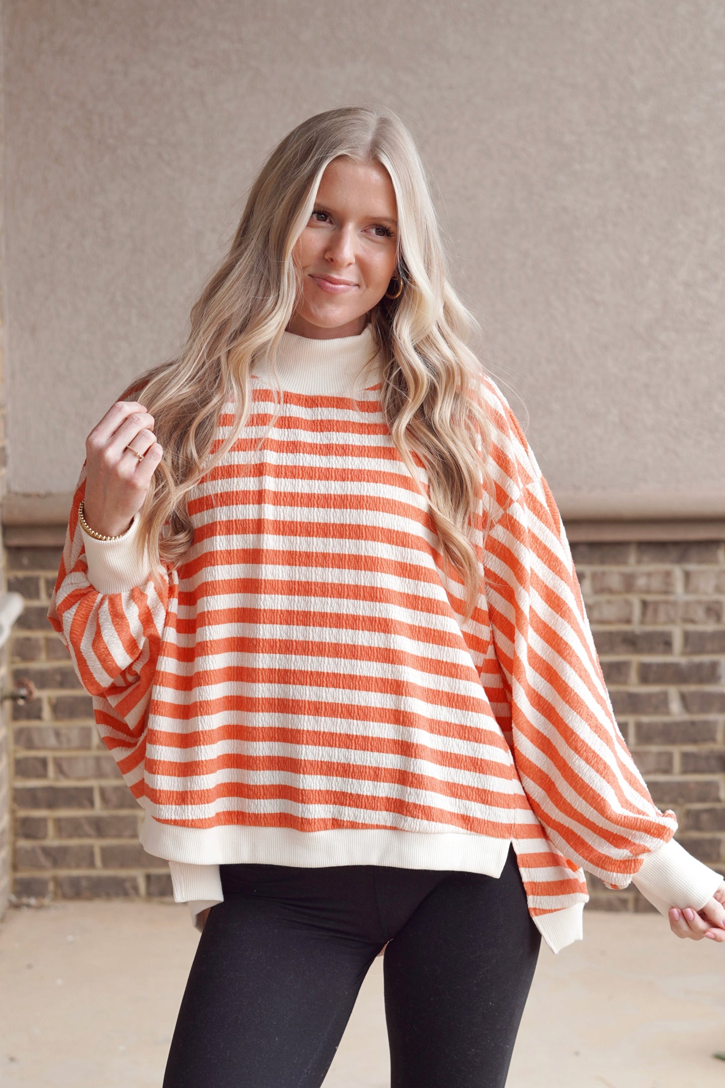Women wearing a orange and cream striped long sleeve flowy mock neck top with some black leggings. 
