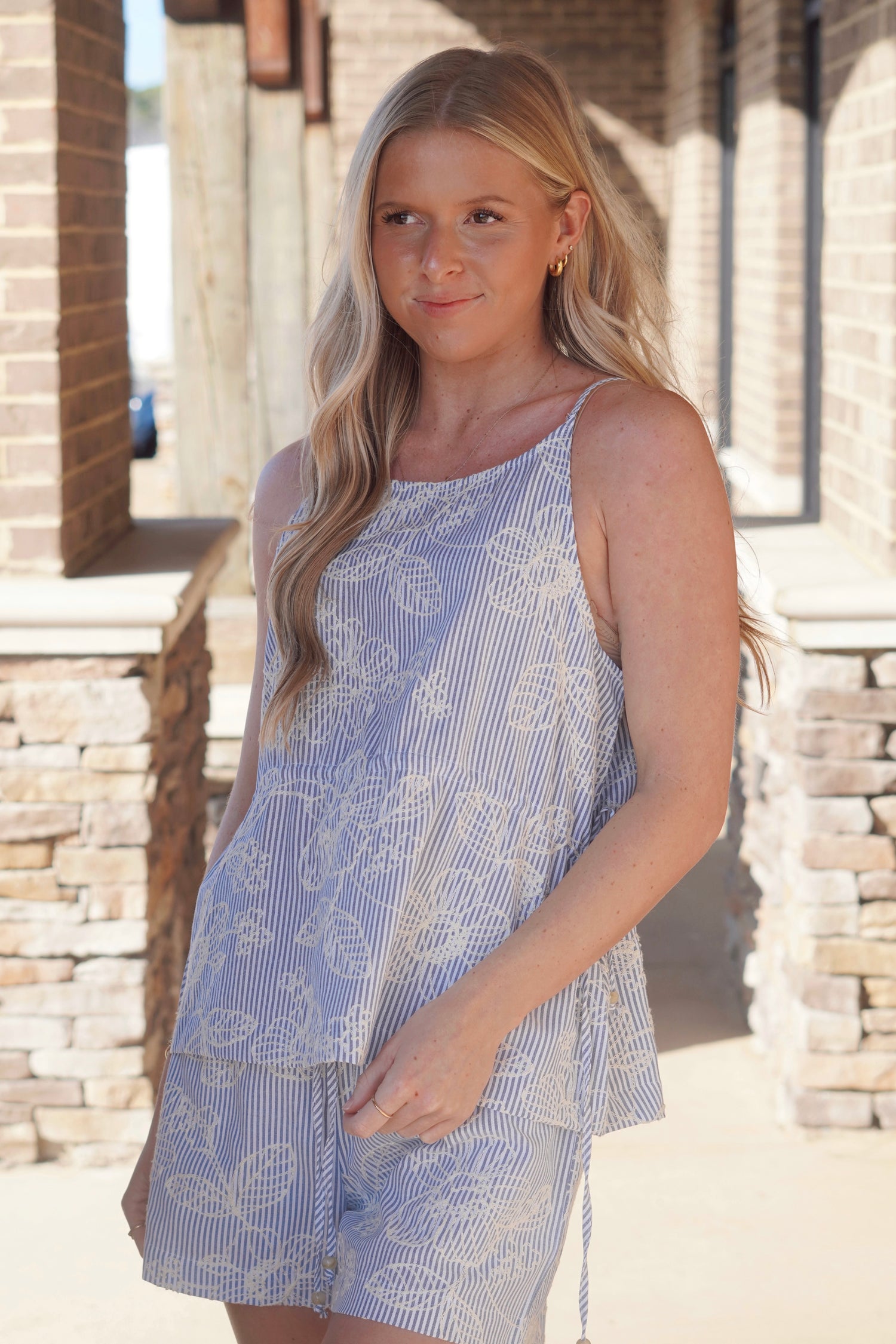 Women wearing a blue and white strip top with a white floral embroidered detail, adjustable cinch waist, spaghetti straps with a round neckline 
