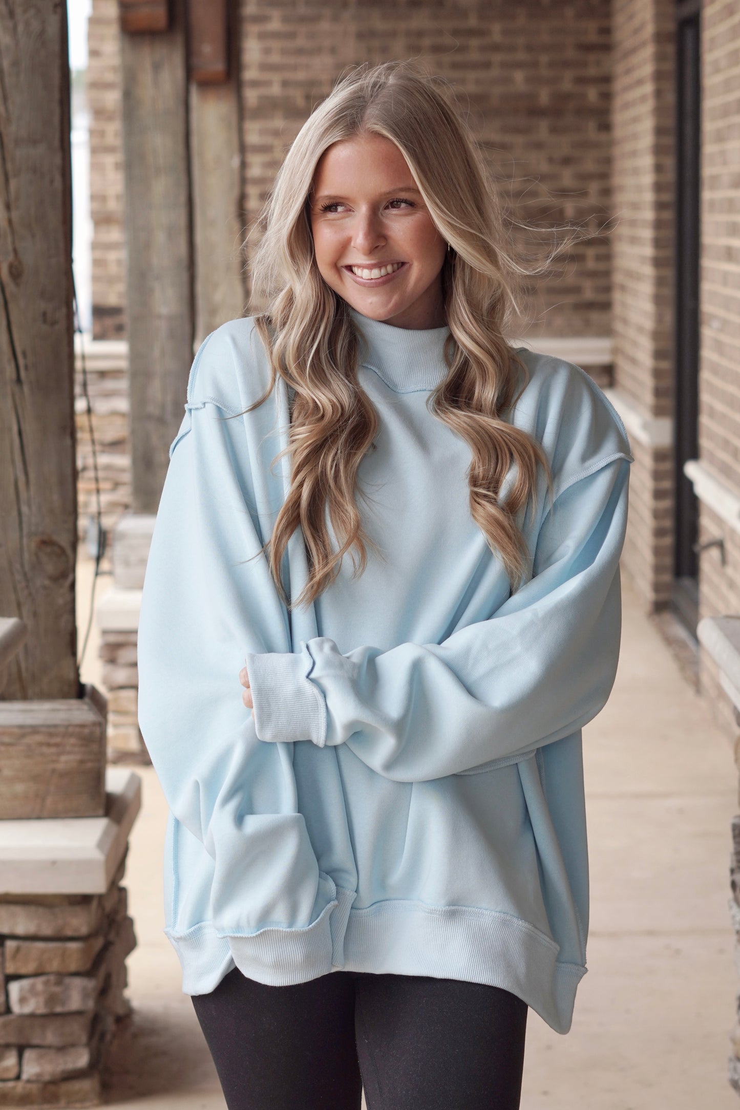 Woman wearing a blue oversized mock neck sweatshirt with black leggings. 