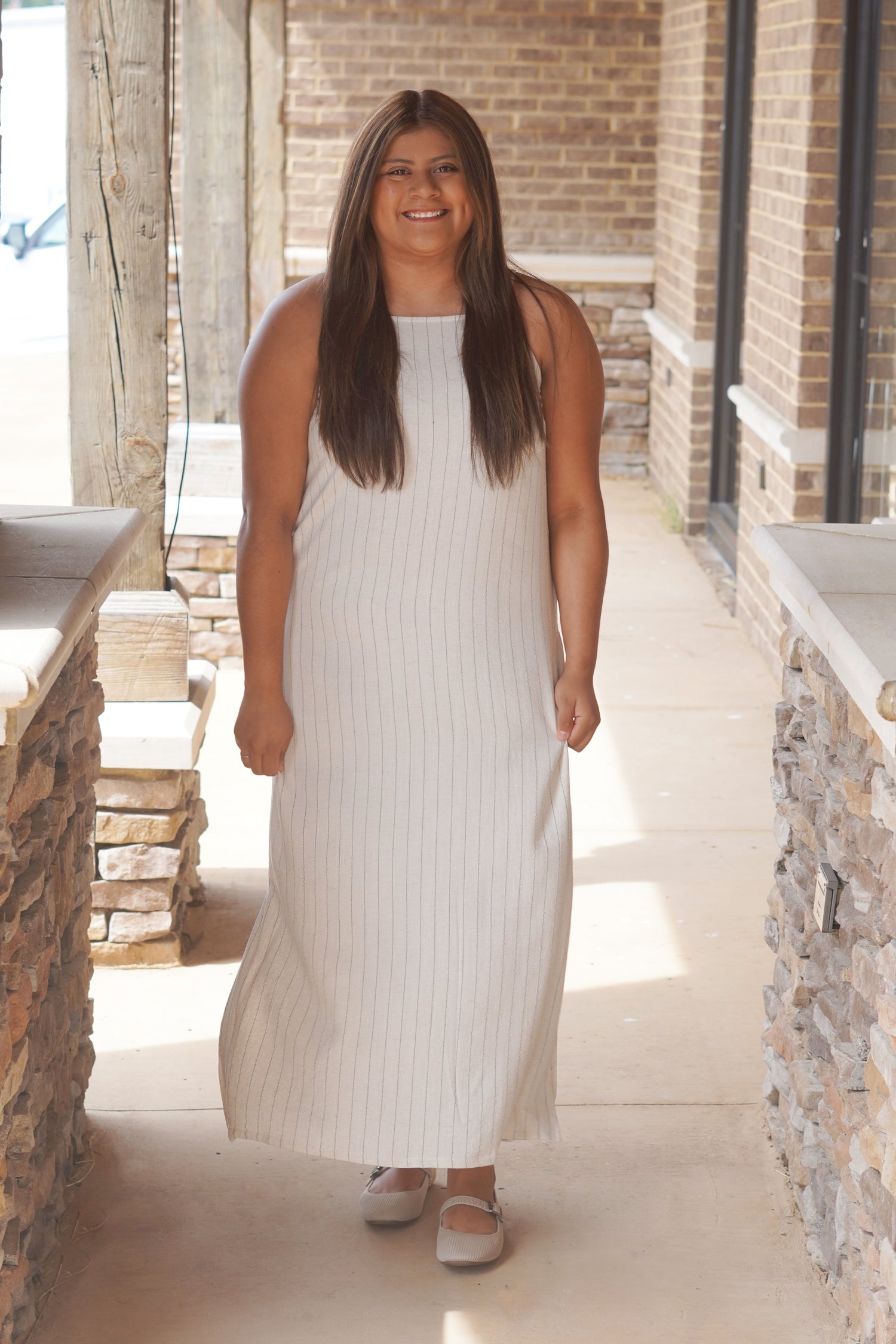 Women wearing a cream pinstripe long dress with a high neckline and it being sleeveless. 