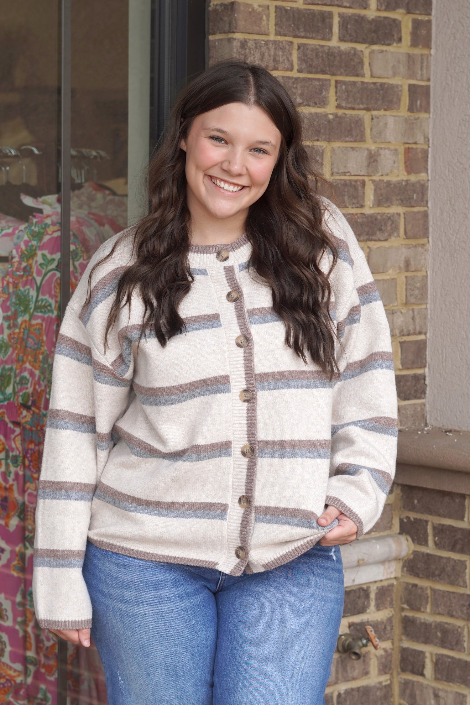 A tan thick cardigan with brown and grey stripes and big brown buttons. 