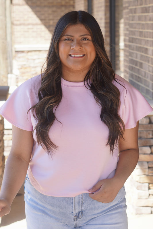 Women wearing a pink top with flutter sleeves, and a round neckline.