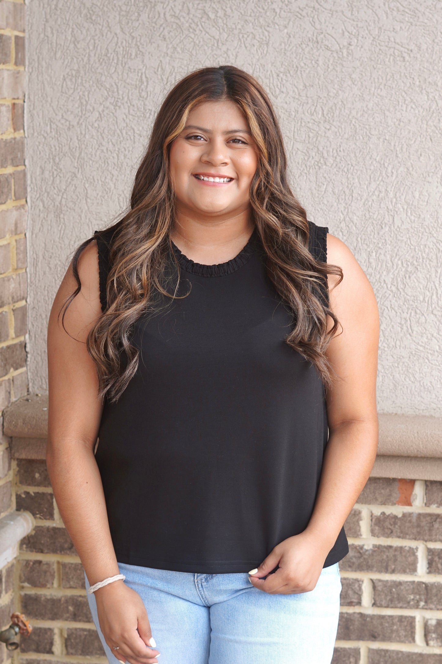 Women wearing a black tank top that has a ruffle trim in the neckline as well as the sleeves, sleeveless, round neckline.