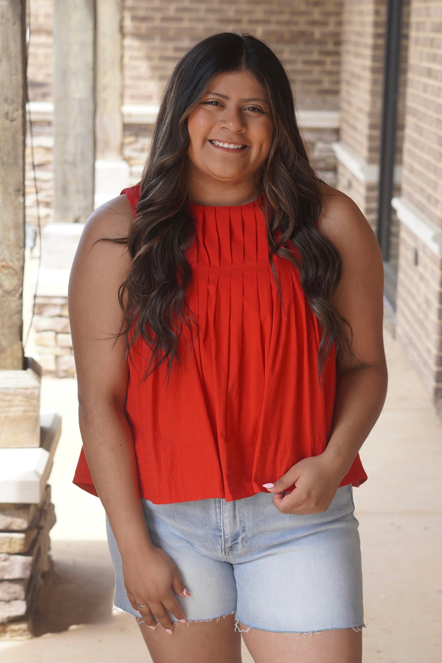 Women wearing a red pleated top with a round neckline, sleeveless. 