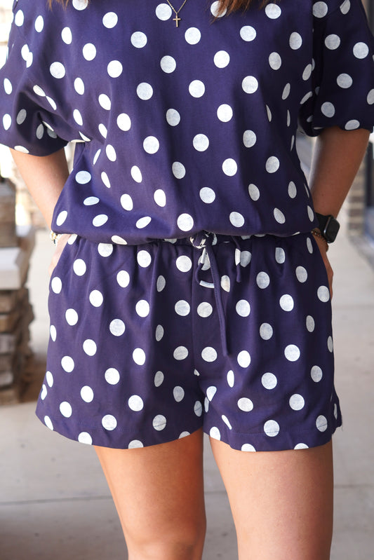 A person wearing a matching navy blue with white polka dot lounge set, featuring a short-sleeve top and drawstring shorts.