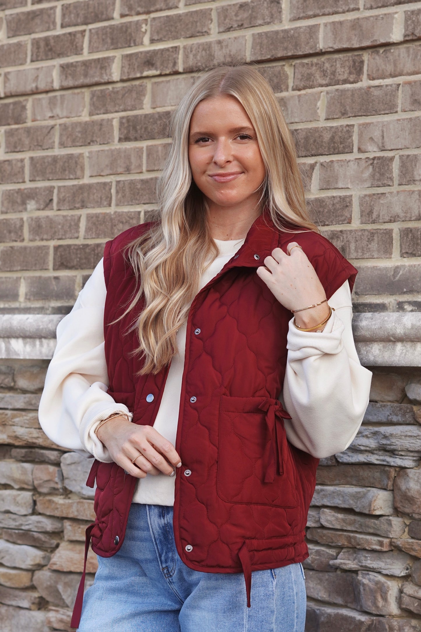 Women wearing a Burgundy Bow Detail Quilted Puffer Vest, Collar Neckline, Snap Button Down, Full Length, Pockets, style with a white crewneck and jeans. 