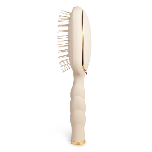 Oval hair brush, beige handle, gentle glide bristle, textured handle with gold trim shown from the side. 
