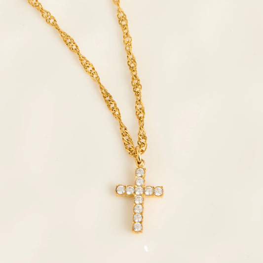 A gold cross pendant necklace adorned with small clear stones, hanging from a gold chain on display.