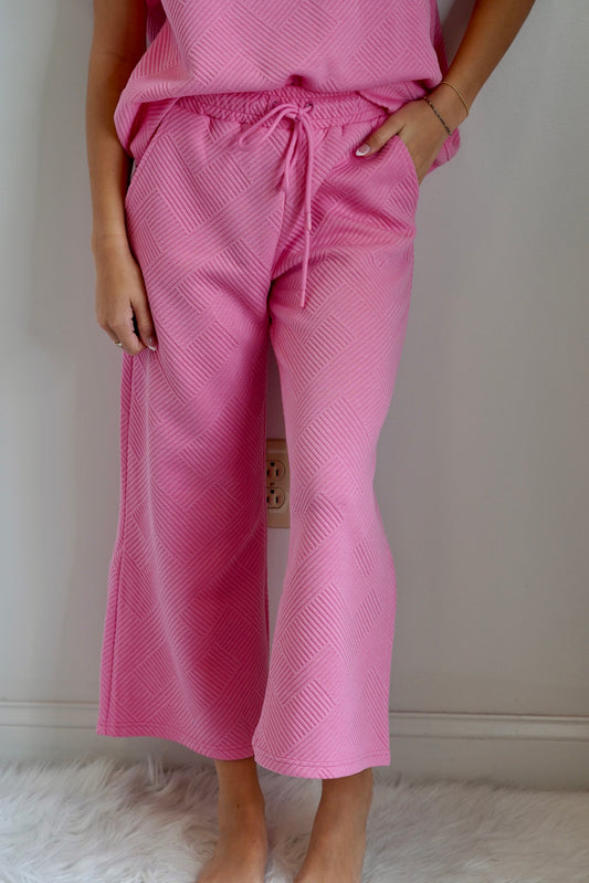 You and your bestie signed up for an outdoor yoga class, now that the heat has died down, but you have no idea what to wear. Don’t worry girlfriend, simply throw on Maci Textured Cropped Pants, and get your downward dog on.  Maci Textured Cropped Pants Wide Legged Bubble Gum Pink Pairs with a Matching Top 83% Polyester  15% Rayon 2% Spandex  Hand Wash, Do Not Bleach, Tumble Dry Low, Low Iron If Needed
