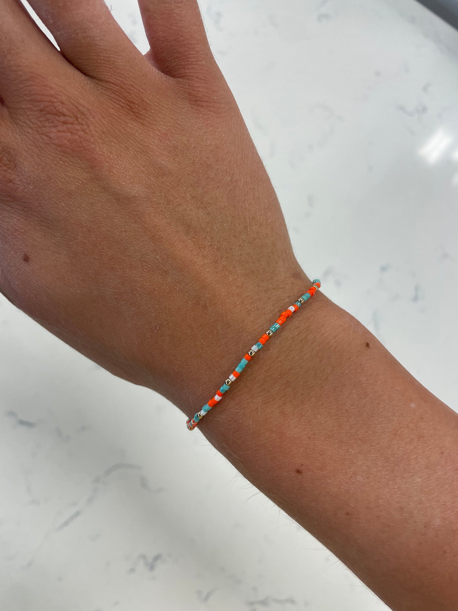 stretchy beaded bracelet with orange, turquoise, white, and gold beads 