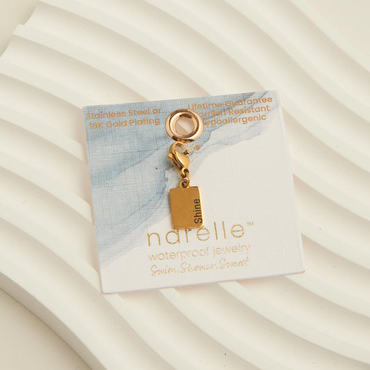 Gold rectangle charm with the word shine written,with a lobster clap.