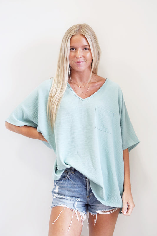 Verity V-Neck Pocket Blouse V Neckline Short Sleeves Pocket on left side of chest Color/Aloe Full length fit 100% Polyester Hand wash with cold water, do not bleach. Hang or line dry. Low iron Model is wearing a size small