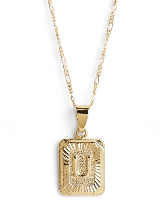 Gold necklace and rectangular charm with the letter U and decretive print on it