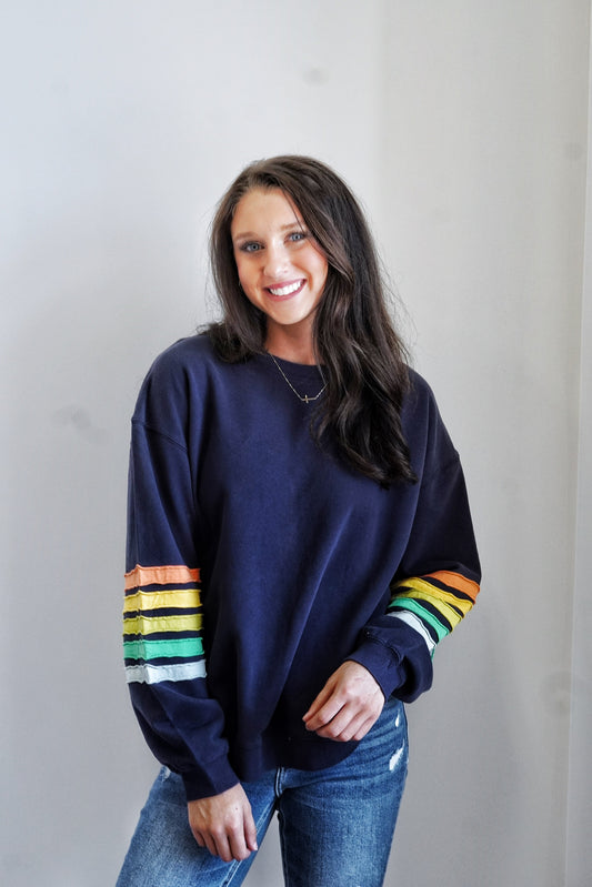 Sadie Striped Sleeve Crew Neck Crew Neckline Long Cuffed Sleeves Colorful Stripes on Sleeve Base Color: Navy Stripe Colors: Orange, Yellow, Green, White Relaxed Fit Full Length 100% Cotton