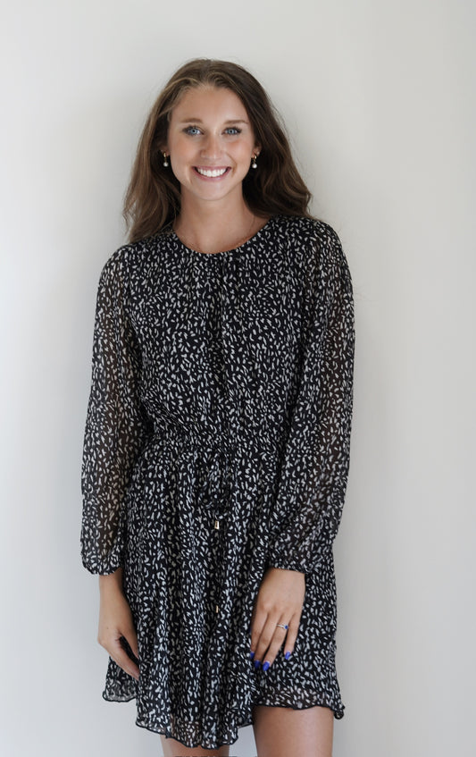 Polly Printed Long Sleeve Dress Round Neckline Long Sleeve, Elastic On End Of Sleeve White Speckle Printed Detail Color: Black  Knee Length Elastic Waistband With Drawstring Tie Flowy Dress 100% Polyester